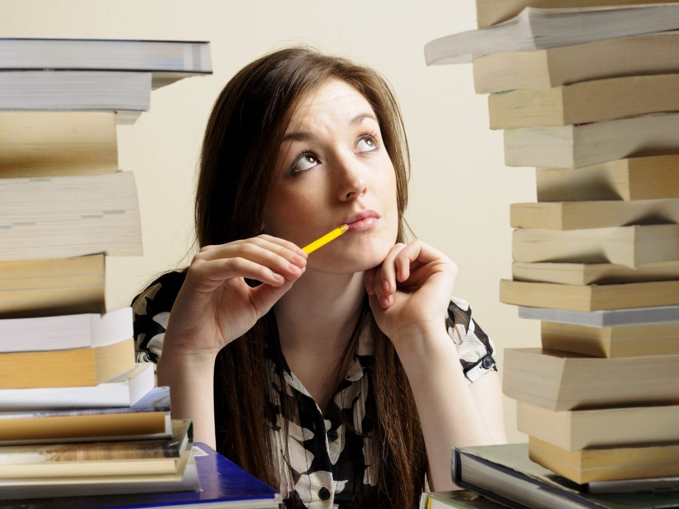 ragazza che pensa con matita in bocca circondata da libri